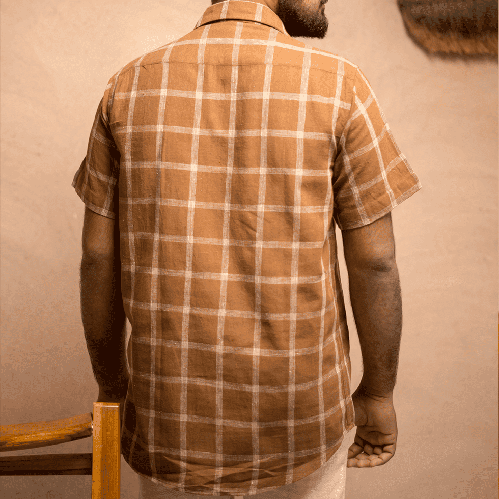 Back view of a man wearing a brown checkered shirt in a rustic setting.