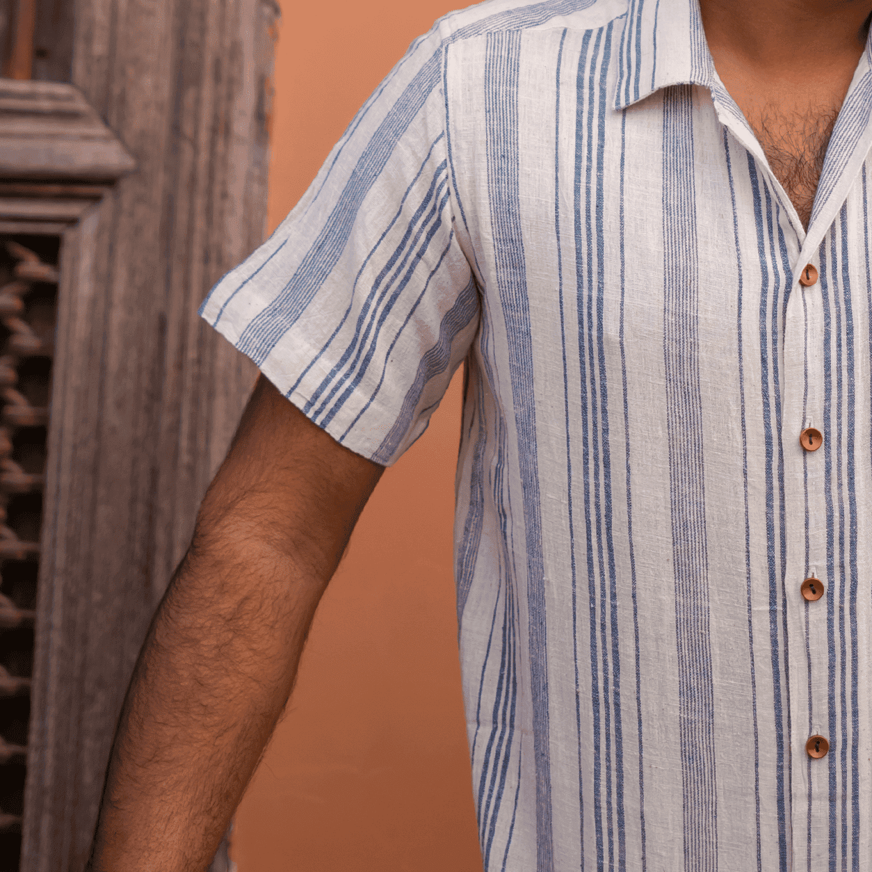 Close-up of a man wearing a striped linen shirt with wooden buttons.