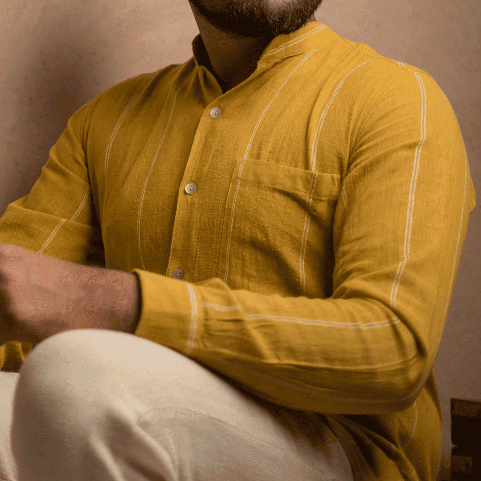 Man wearing a mustard yellow kurta with white pants, sitting with arms crossed.