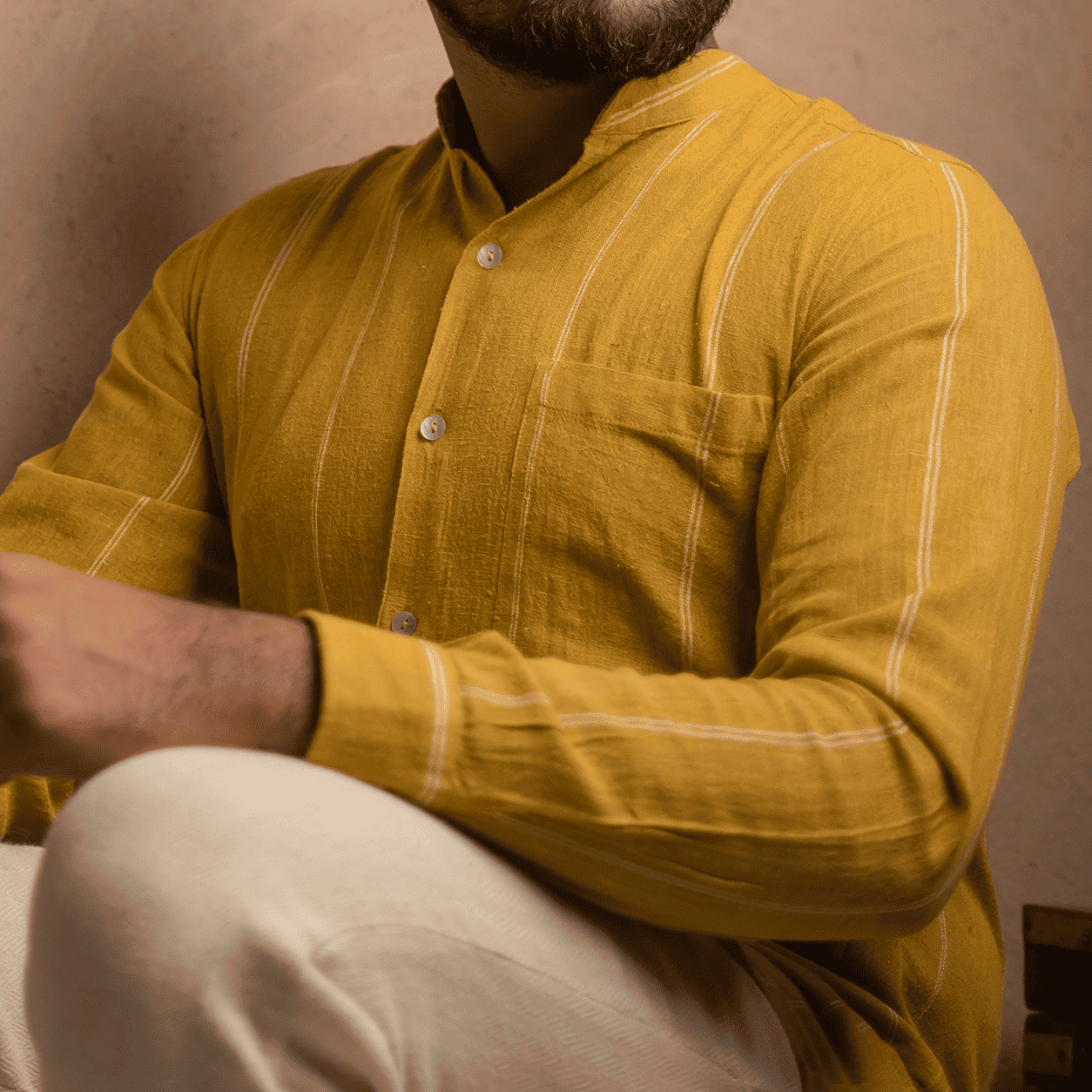 Man wearing a mustard yellow kurta with white pants, sitting with arms crossed.