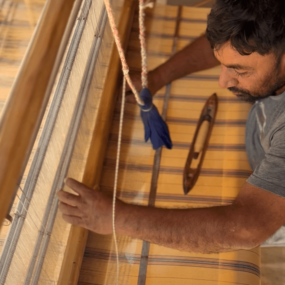 Man working on traditional wooden loom with yellow and brown fabric.
